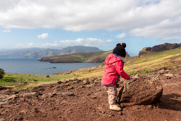 Small toddler with scenic view of majestic Atlantic Ocean coastline at Ponta de Sao Lourenco peninsula, Canical, Madeira island, Portugal, Europe. Coastal hiking trail along steep rocky rugged cliffs