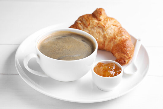 Fresh croissant, jam and coffee on white wooden table. Tasty breakfast