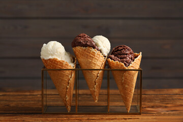 Tasty ice cream scoops in waffle cones on wooden table, closeup