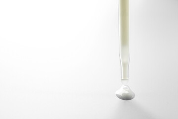 Dripping moisturizing serum from pipette on light grey background, closeup. Space for text