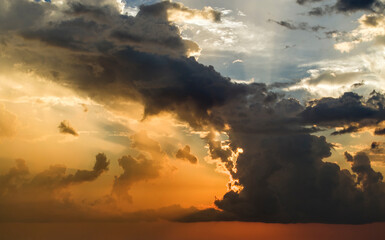 Bright sunset with setting sun behind vivid orange and yellow clouds