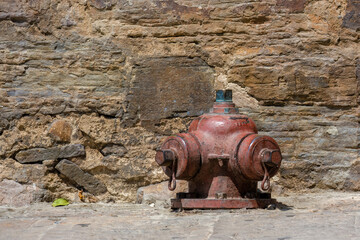 A very old hydrant half buried in a street of the colonial town of Villa de Leyva, in central Colombia, against a stone wall.