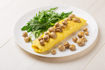 French three eggs omelette with mushrooms, arugula for a breakfast on a white plate on wooden...