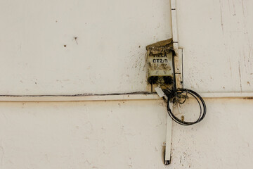 A rusty, weathered and neglected cable connection box in a dirty white wall, in the colonial town of Villa de Leyva, in central Colombia.