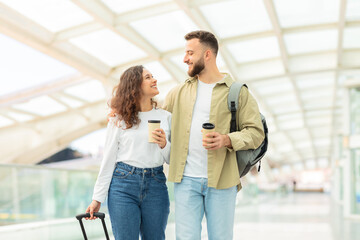 Smiling duo holding coffee at transport hub