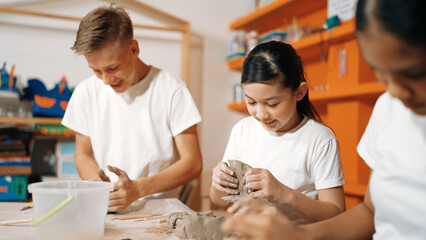 Caucasian boy modeling bowl of clay while cute asian girl working on dough at pottery workshop. Skilled highschool student playing on dough while wear muddy shirt at art lesson. Creative. Edification.