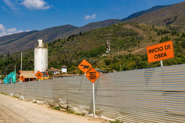 The metal protective wall of a construction site, with warning signs in Spanish: "work start", "walk on the front sidewalk", "drive with caution", in the town of Villa de Leyva.