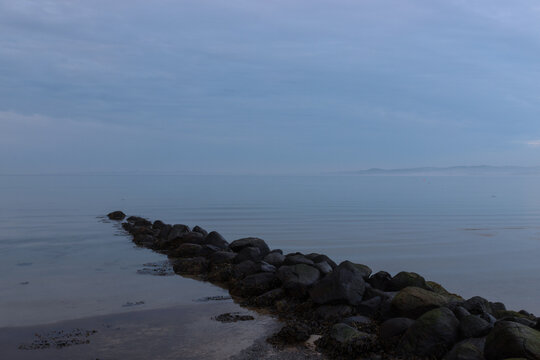 Tranquil seascape with stone pier and cloudy sky.