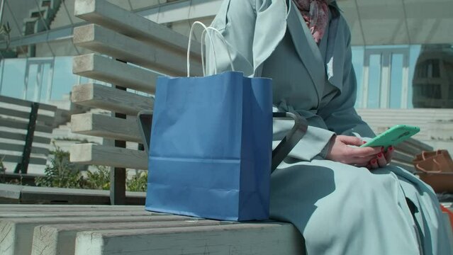 The woman sitting on a bench with a lot of shopping bags, man stealing her purse and bag while she is sitting with her phone and checking her emails.