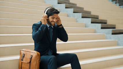 Professional business man picking and listening music by using headphone while sitting at stairs....