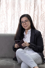 Retrato de joven mujer con lentes latina emprendedora, trabajando desde casa feliz con celular