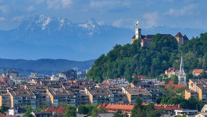AERIAL: Historic Ljubljana castle overlooks the downtown beneath the mountains. - obrazy, fototapety, plakaty