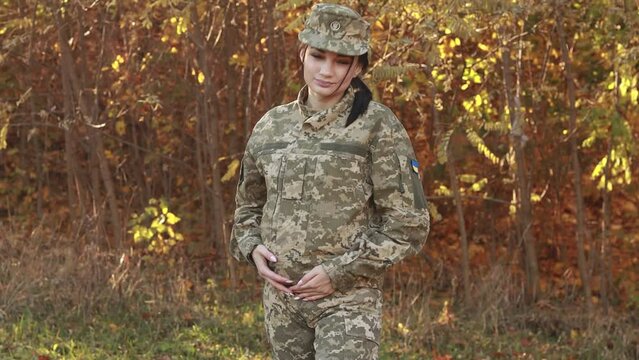 Pregnant female servicewoman soldier strokes her belly, dressed in the camouflage military uniform, patch symbol of independence. Armed Forces of Ukraine. Woman serving in ukrainian army

