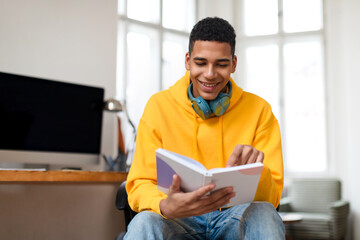 Happy teen guy reading book with headphones on