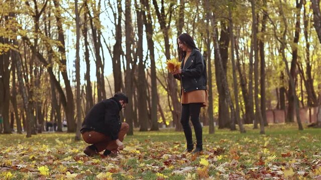 Young loving couple walking outside in the city park in sunny weather, collect orange yellow red maple leaves, hugging smiling kissing laughing spending time together. Autumn, fall season 