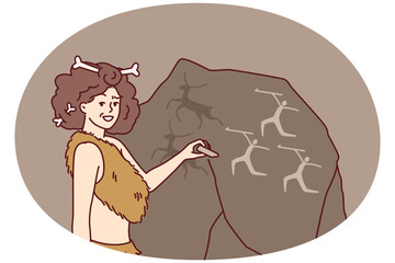 Ancient woman in clothing made from animal skins and bones in hair makes rock paintings. Girl depicts people hunting deer on giant stone and smiling looks at screen
