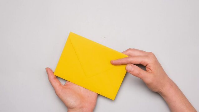 A hand pulls out a white card from a bright yellow envelope. Top view of a yellow envelope on gray background. Banner for social media ad with copy space