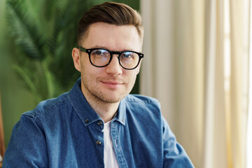 A poised young man with glasses offers a confident gaze, the verdant backdrop complementing his...