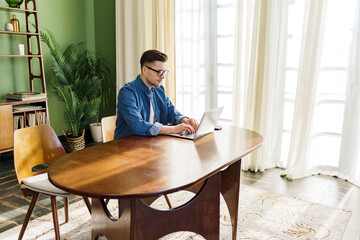 A focused individual diligently attends to his laptop in a room suffused with the tranquility of...