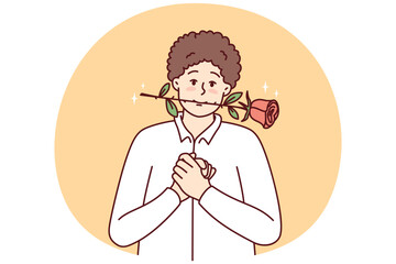 Timid young guy with rose in mouth clenching palms in front of chest looks at screen with head tilted to side. Man in white shirt hopes girl will like him and invite lover on date
