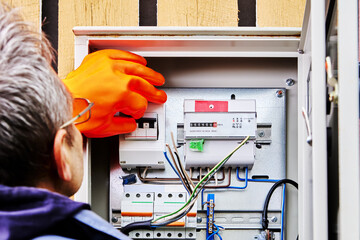 An electrician wearing protective dielectric gloves turns off power supply to circuit breaker in an...