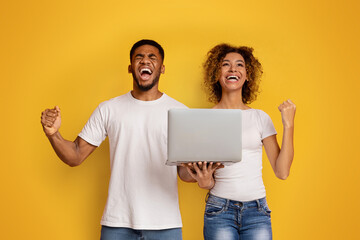 Joyful couple celebrating with laptop on yellow background