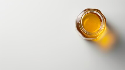 Amber honey in a transparent glass jar isolated on light background. Top view. Concept of simplicity, natural sweeteners, and bee products. Banner. Copy space - obrazy, fototapety, plakaty