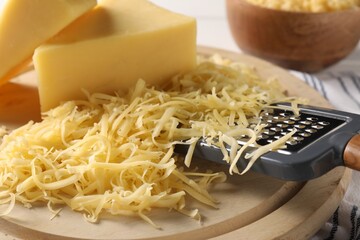 Grated, whole pieces of cheese and grater on board, closeup