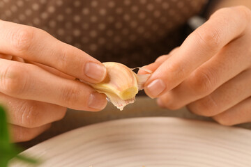 Woman peeling fresh garlic at table, selective focus