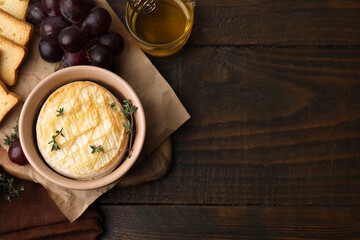 Tasty baked camembert in bowl, grapes honey and croutons on wooden table, flat lay. Space for text