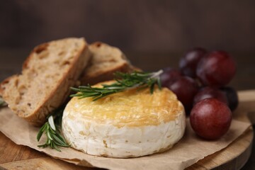 Tasty baked camembert, pieces of bread, grapes and rosemary on table, closeup