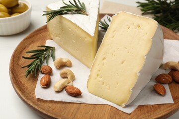 Plate with pieces of tasty camembert cheese, nuts and rosemary on table, closeup