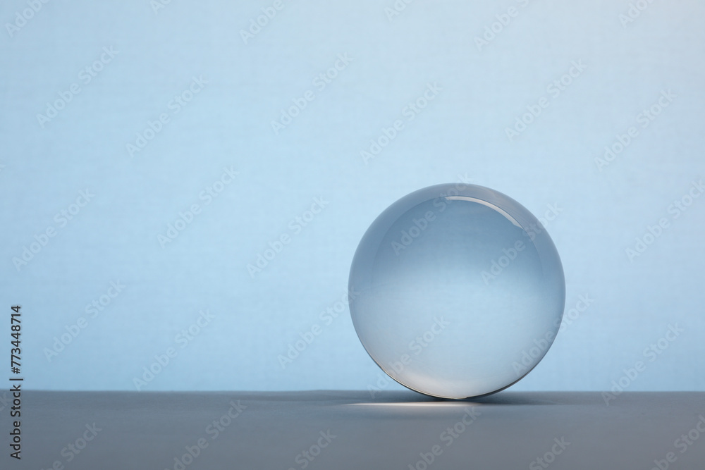 Poster Transparent glass ball on table against light blue background. Space for text