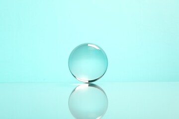 Transparent glass ball on mirror surface against turquoise background