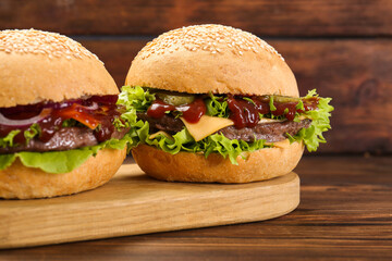 Board with delicious cheeseburgers on wooden table, closeup