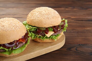 Board with delicious cheeseburgers on wooden table, closeup. Space for text
