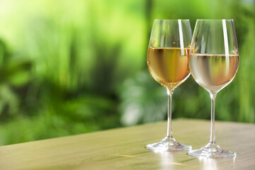 Tasty white wine in glasses on wooden table, space for text