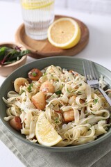 Delicious scallop pasta with spices and lemon in bowl served on white table, closeup