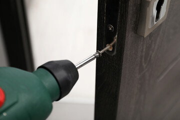 Handyman with electric screwdriver repairing door handle indoors, closeup