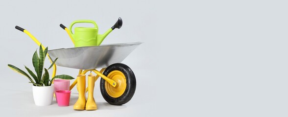 Wheelbarrow with plant and gardening supplies on light background with space for text
