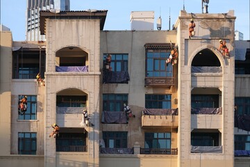 A group of workers hanging on ropes are painting the facade of a building. Souk Al Bahar, Dubai