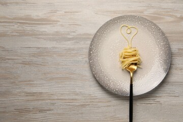 Heart made with spaghetti and fork on light wooden table, top view. Space for text