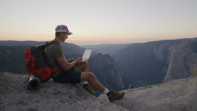 Young hiker with red backpack sitting on the summit of mountain range, looking in the distance, observing amazing view of dark rocks on summer evening. High quality 4k footage