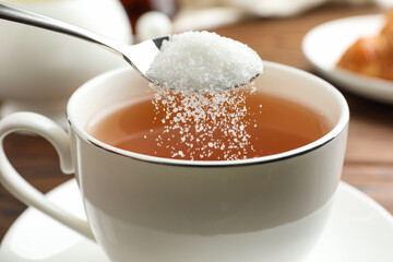 Adding sugar into cup of tea at table, closeup