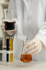 Laboratory worker holding beaker and flask with different types of crude oil at light marble table, closeup