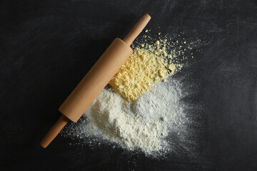 Rolling pin and different types of flour on black table, top view
