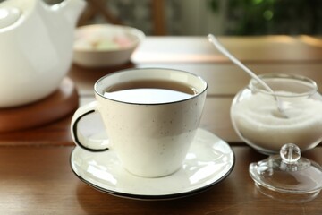 Cup of aromatic tea and sugar on wooden table, closeup