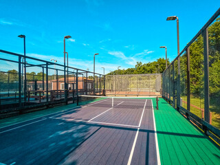 Fototapeta na wymiar Summertime scene of elevated sport courts with nets in a public park setting. Courts are used for paddle tennis or pickleball play. Floor surface is green and blue with white boundary lines.