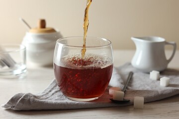 Pouring warm tea into cup on white wooden table, closeup
