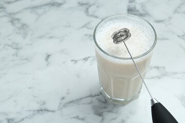 Mini mixer (milk frother) and tasty cappuccino in glass on white marble table, closeup. Space for text © New Africa